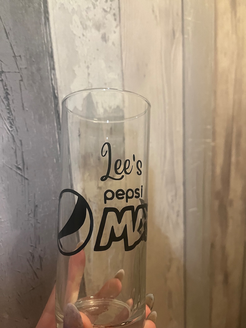 Puede incluir: Un vaso de vidrio transparente con un logotipo de Pepsi negro y el texto "Lee's Pepsi" en &eacute;l.