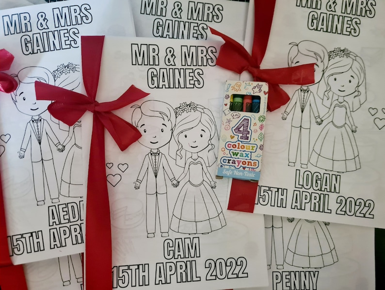May include: Four coloring books with a red ribbon and a pack of crayons. Each book features a cartoon couple with the text "Mr. & Mrs. Gaines" and the date "15th April 2022". The names "Aedi", "Cam", "Logan", and "Penny" are also included.