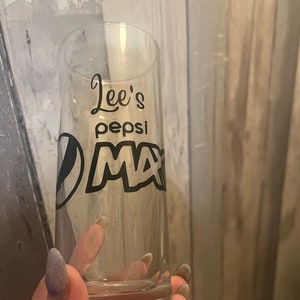 Puede incluir: Un vaso de vidrio transparente con un dise&ntilde;o negro que dice "Lee's Pepsi Max".