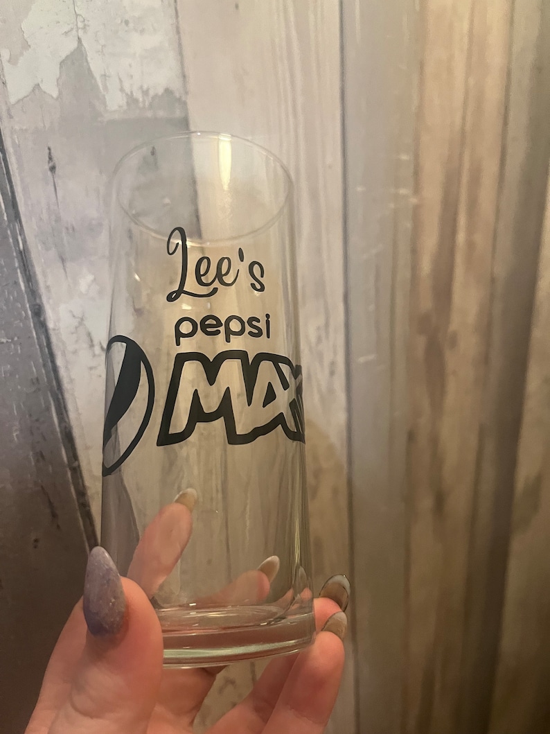 Puede incluir: Un vaso de vidrio transparente con un dise&ntilde;o negro que dice "Lee's Pepsi Max".