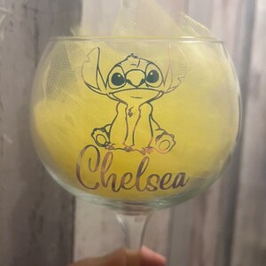 May include: A clear glass with a yellow and white design. The glass features a cartoon character with big eyes and the name "Chelsea" written on the bottom.