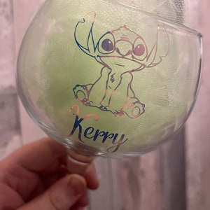 May include: A clear glass with a green and gold design of a cartoon character. The character is Stitch from the Disney movie Lilo & Stitch. The glass has the name "Kerry" written on it.