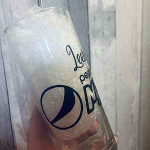 Puede incluir: Un vaso de vidrio transparente con un dise&ntilde;o en blanco y negro que dice "Leeby Pepper" y tiene el logotipo de Pepsi. El vaso est&aacute; lleno de cacahuetes de embalaje blancos.