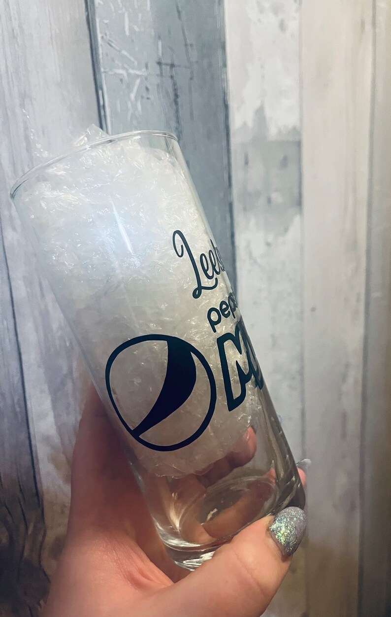 Puede incluir: Un vaso de vidrio transparente con un dise&ntilde;o en blanco y negro que dice "Leeby Pepper" y tiene el logotipo de Pepsi. El vaso est&aacute; lleno de cacahuetes de embalaje blancos.