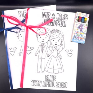 May include: A coloring book with a bride and groom on the cover. The book is titled "Mr. & Mrs. Jameson" and the date "15th April 2023". The book is tied with a pink and blue ribbon. A pack of four color crayons is included.