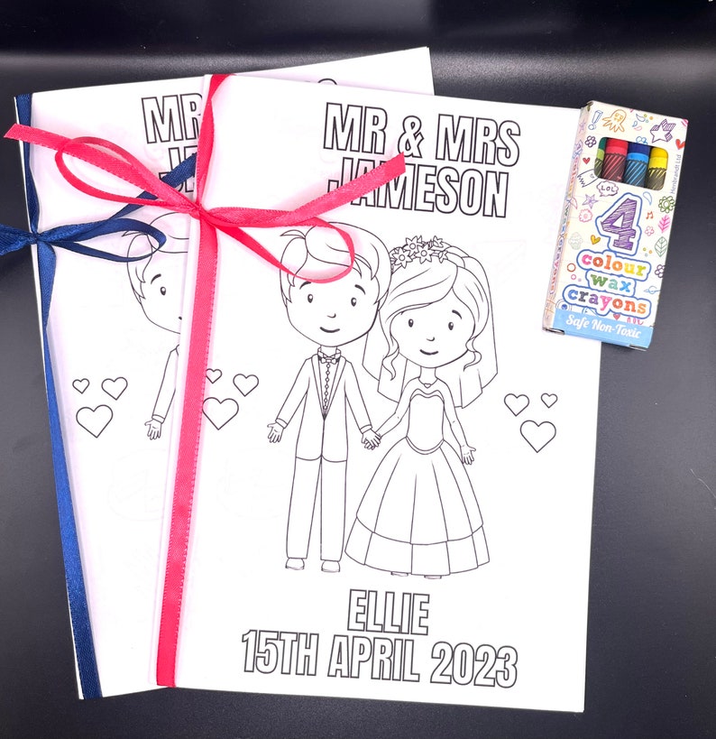 May include: A coloring book with a bride and groom on the cover. The book is titled "Mr. & Mrs. Jameson" and the date "15th April 2023". The book is tied with a pink and blue ribbon. A pack of four color crayons is included.