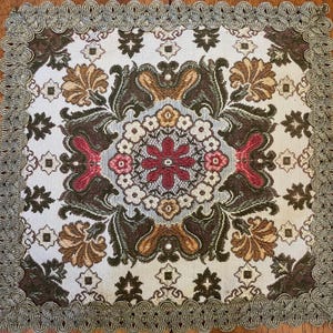 May include: A square fabric doily featuring a central floral medallion in shades of red, white, and light blue, surrounded by dark green and gold leaf patterns on a cream background, finished with a decorative gold scalloped lace border.