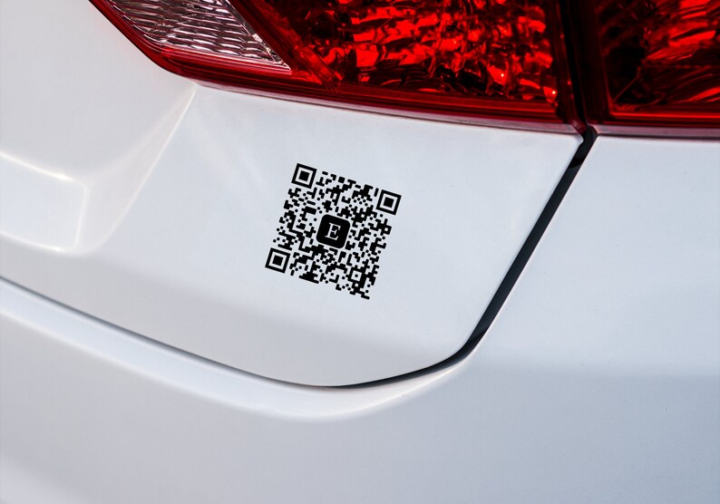 May include: A white car with a black QR code sticker on the back bumper. The QR code has a letter "E" in the center.