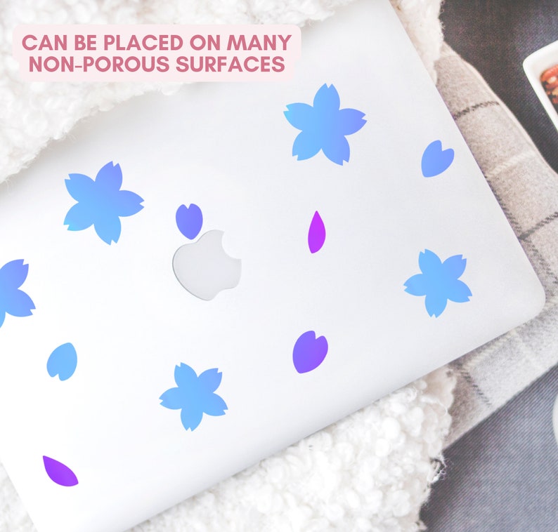May include: A white laptop adorned with blue and purple flower and petal-shaped decals. The text "CAN BE PLACED ON MANY NON-POROUS SURFACES" is displayed in pink. The decals are arranged across the laptop's surface.