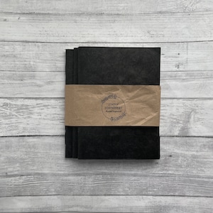 May include: Three black notebooks with a brown paper band around them. The band has a logo that says "Simply Stationery" and "Handcrafted".