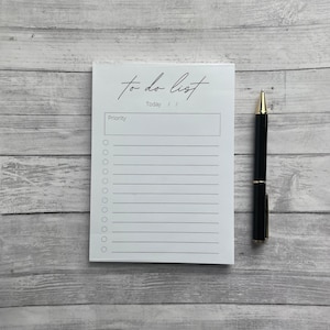 May include: A white to-do list notepad with a black pen. The notepad has a black handwritten title "to do list" and the word "Today" written below it. The notepad has a section labeled "Priority" and 15 lines for writing tasks.