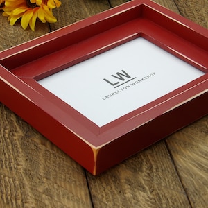 May include: A red wooden picture frame with a white mat and the text "LW LAURELTON WORKSHOP" printed on the mat.
