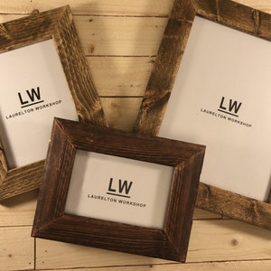 May include: Three rustic wooden picture frames in different sizes, all with a dark brown stain. Each frame has a white mat and features the text "LW LAURELTON WORKSHOP" printed in black.