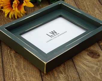 May include: A dark green picture frame with a white border and the text "LW LAURELTON WORKSHOP" on the inside.