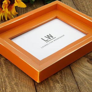 May include: Orange wood picture frame with a white mat and the text "LW LAURELTON WORKSHOP" printed on the mat.