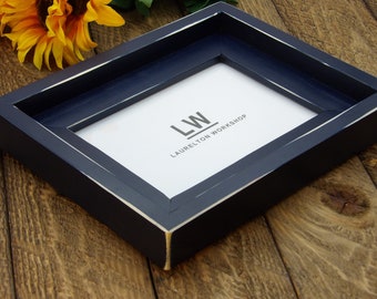 May include: A navy blue picture frame with a white distressed finish. The frame has a white mat and the text "LW LAURELTON WORKSHOP" is printed on the mat.