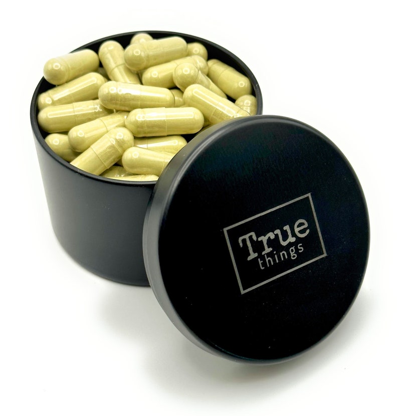 May include: A black metal container filled with light green capsules. The container has a lid with the words "True things" printed on it.