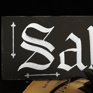 May include: Black chalkboard sign with the word "Sale" written in white paint in a gothic font.
