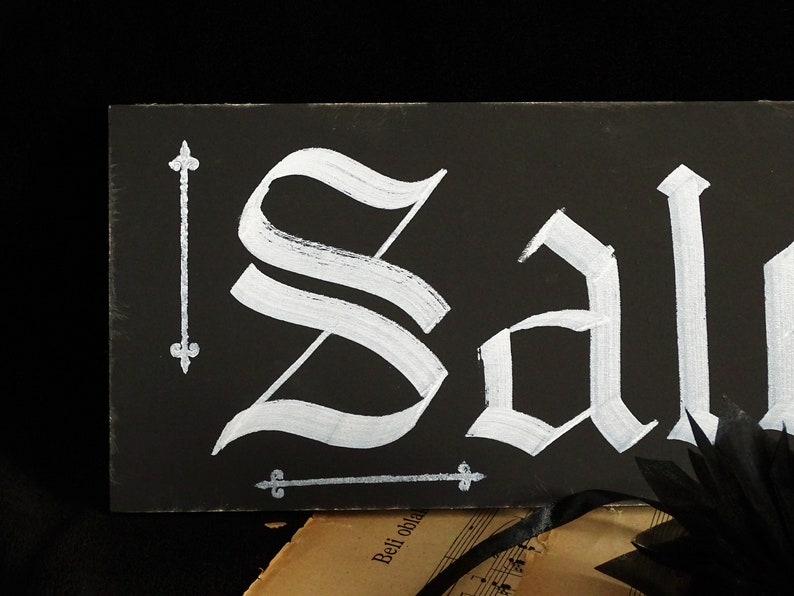 May include: Black chalkboard sign with the word "Sale" written in white paint in a gothic font.