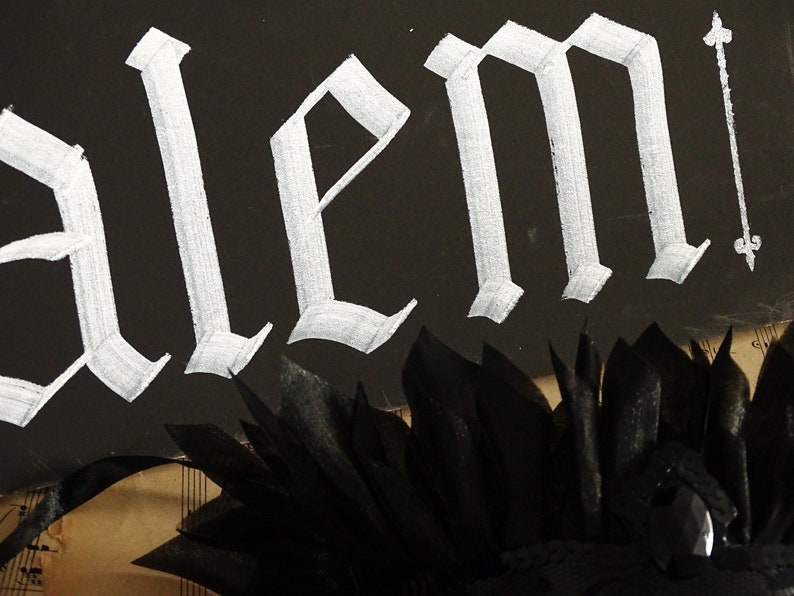 May include: A black background with the word "alem" written in white gothic script. A black feather boa is at the bottom of the image.