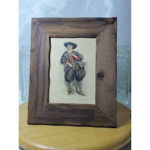 May include: A framed print featuring a colorful illustration of a man in historical attire. The print is set within a rustic, dark brown wooden frame. The man is wearing a hat, jacket, and breeches. The frame has a natural, textured appearance.