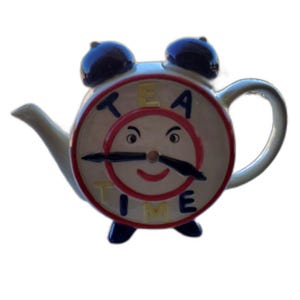 May include: A ceramic teapot shaped like an alarm clock with a cream-colored body, dark blue bells on top, and dark blue feet. The face features a smiling expression, black clock hands, and the yellow text TEA TIME printed on the front.