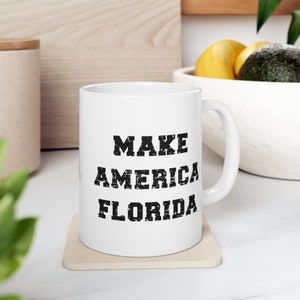 May include: White ceramic mug with a black graphic that reads "MAKE AMERICA FLORIDA".