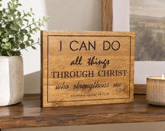 May include: A rectangular wooden sign with a natural brown finish and a thin black border. The text engraved in black reads: I CAN DO all things THROUGH CHRIST who strengthens me PHILIPPIANS 4:13. The sign features a mix of serif and script fonts.
