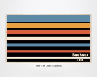 May include: A framed art print featuring a Bauhaus design with horizontal stripes in blue, orange, red, cream, and black. The text "Bauhaus 1923" is displayed in white. The artwork is framed in a light wood-colored frame.