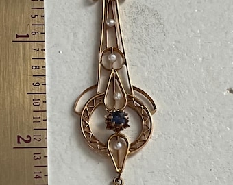 May include: A gold-toned pendant with an Art Nouveau design. It features a central blue gemstone, small pearls, and a teardrop-shaped pearl at the bottom. The pendant is approximately 3.5 inches long.