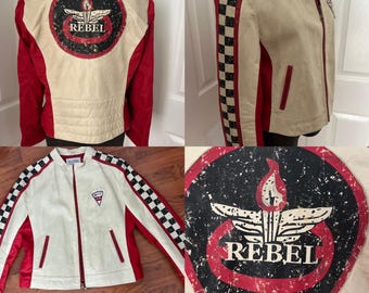 May include: A cream-colored jacket with red accents and a black and white checkered pattern on the sleeves. The back features a large circular emblem with the word "REBEL" and a flame design. The jacket has a zipper closure and two front pockets.