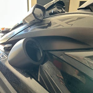 May include: A matte black personal watercraft featuring a side-mounted rearview mirror, a circular speaker housing, and a prominent FX logo on the side panel. The body displays a sleek, angular design with visible screw fasteners and a dark finish.