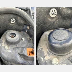 Puede incluir: Primer plano del compartimento del motor de un coche que muestra dos tapas de goma negras con un símbolo en forma de estrella en cada una. Las tapas están situadas en la parte superior del bloque del motor.
