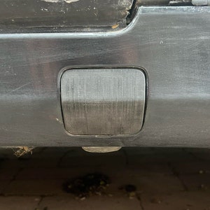 May include: A black plastic rectangular rear bumper reflector on a black car.