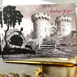 Könnte beinhalten: Eine Schwarzweiß-Vintage-Illustration einer Frau, die einen Hund vor einem steinernen Schloss spazieren führt. Der Text "Thinking of you" ist in rosa Kursivschrift oben auf der Karte geschrieben.