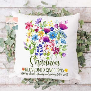 May include: White pillow with a colorful floral design and the text "Shannon Blossomed Since 1945 Adding a touch of beauty and sweetness to the world".