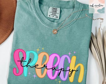 May include: A teal Comfort Colors t-shirt with the words "speech therapy" in colorful, bubble letters. The word "therapy" is written in cursive. A gold necklace with a pendant is draped on the shirt.