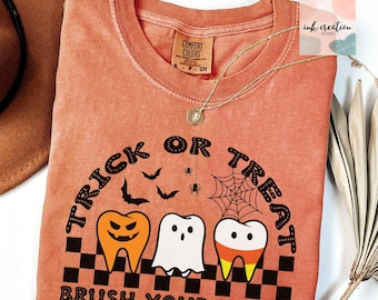 May include: A burnt orange t-shirt with a black and white graphic that says "Trick or Treat Brush Your Teeth". The graphic features three teeth with Halloween-themed decorations. One tooth has a jack-o-lantern face, another is a ghost, and the third has a candy corn design.