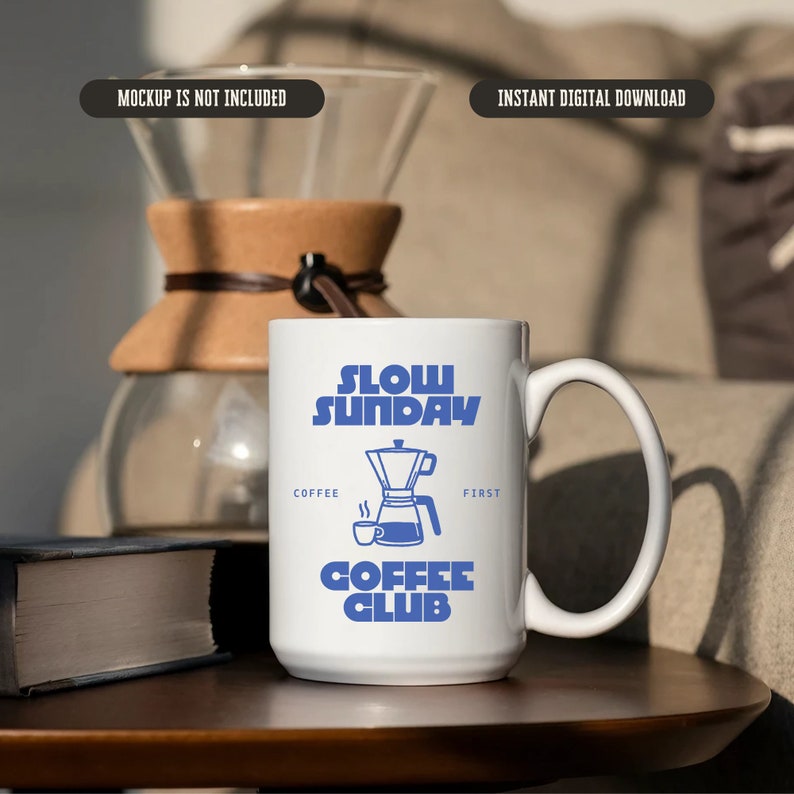 May include: White ceramic coffee mug with blue text that reads "Slow Sunday Coffee Club" and a blue illustration of a coffee pot. The mug is on a wooden table.