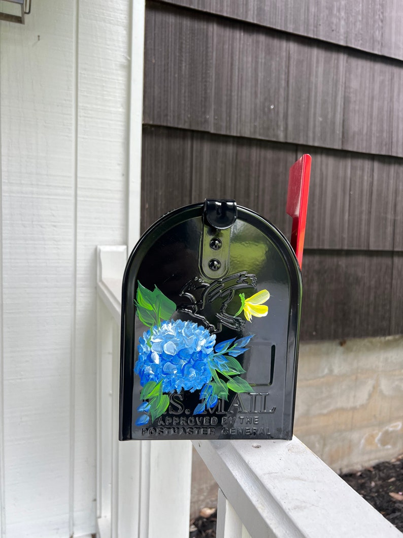 Puede incluir: Buz&oacute;n negro con un dise&ntilde;o floral azul y amarillo. El buz&oacute;n tiene el texto "U.S. MAIL APPROVED BY THE POSTMASTER GENERAL" en la parte delantera.