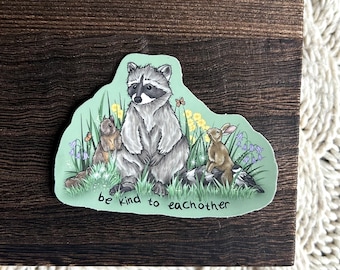 May include: A sticker featuring a raccoon, squirrel, rabbit, and bird in a grassy scene with flowers and butterflies. The text "be kind to each other" is written on the sticker.