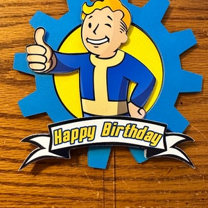 May include: A blue and yellow birthday cake topper featuring a cartoon character giving a thumbs up. The character is set against a blue gear shape and a yellow circle. The words "Happy Birthday" are displayed on a banner.