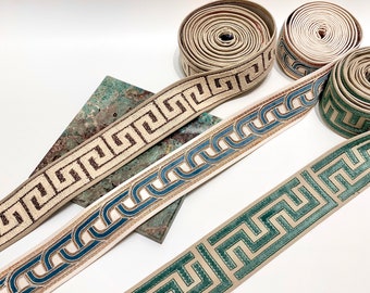 Pode incluir: Três rolos de guarnição decorativa com padrões geométricos. A guarnição é em tons de bege, castanho, azul e verde.