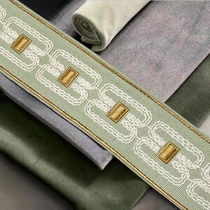 Pode incluir: Um close-up de uma guarni&ccedil;&atilde;o de tecido verde e branco com um padr&atilde;o de corrente dourada. A guarni&ccedil;&atilde;o &eacute; tecida com uma textura sutil e apresenta um desenho repetitivo de correntes entrela&ccedil;adas.