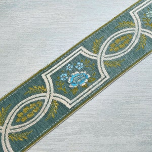 May include: A teal blue ribbon with a white and gold floral pattern. The pattern features stylized flowers and leaves.
