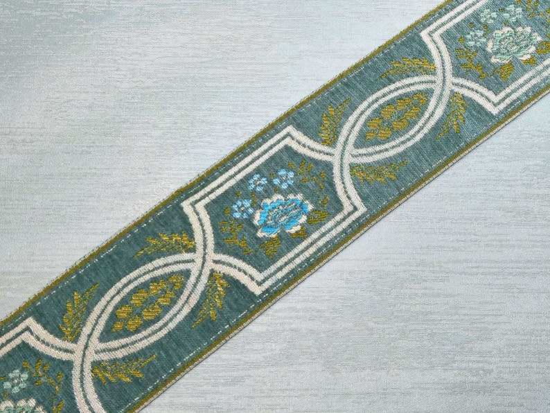 May include: A teal blue ribbon with a white and gold floral pattern. The pattern features stylized flowers and leaves.