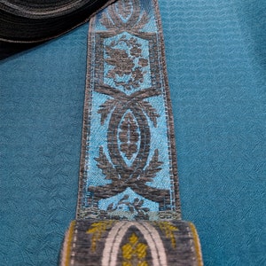 May include: A roll of blue and gray patterned trim with a floral design. The trim is rolled up and the end is visible.