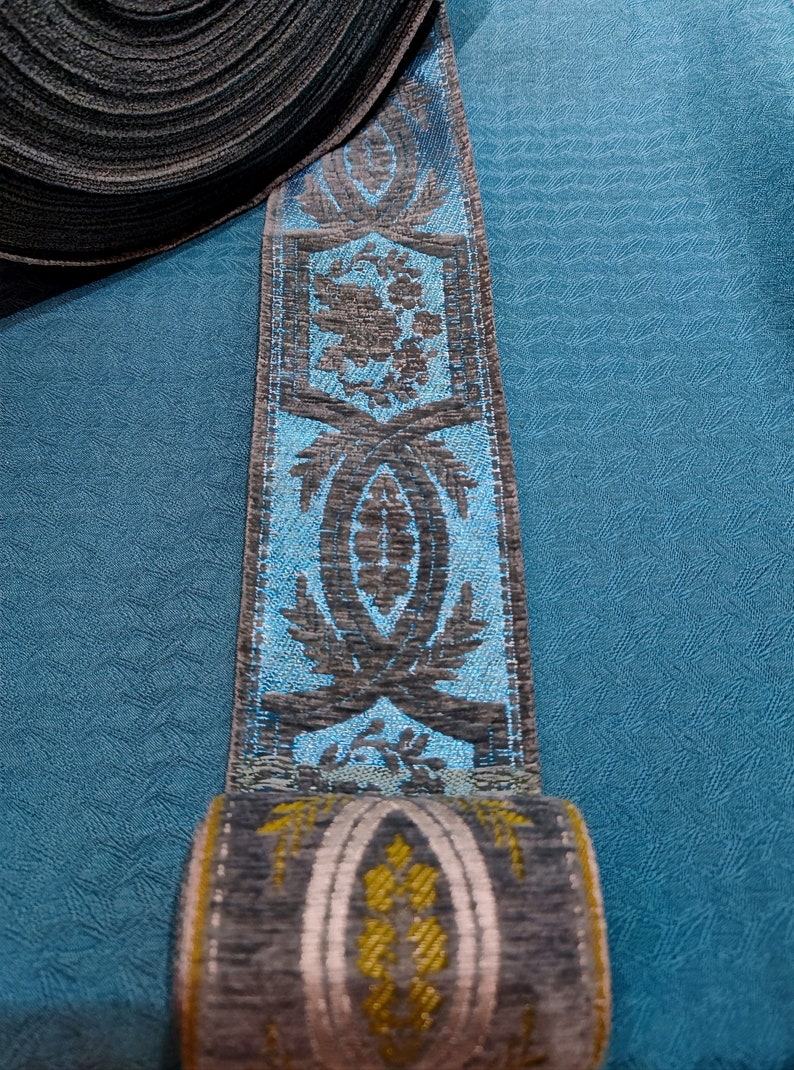 May include: A roll of blue and gray patterned trim with a floral design. The trim is rolled up and the end is visible.