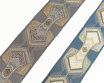 Pode incluir: Duas faixas de tecido decorativas com desenhos geométricos. Uma é cinza com detalhes em bege e marrom, a outra é azul com detalhes em creme e bege. Os desenhos apresentam formas de diamantes e quadrados com detalhes intrincados.