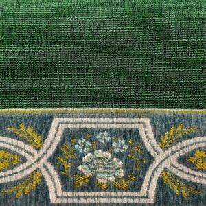 May include: Close-up of a green fabric with a decorative border. The border features a floral design with white and gold accents on a blue background.